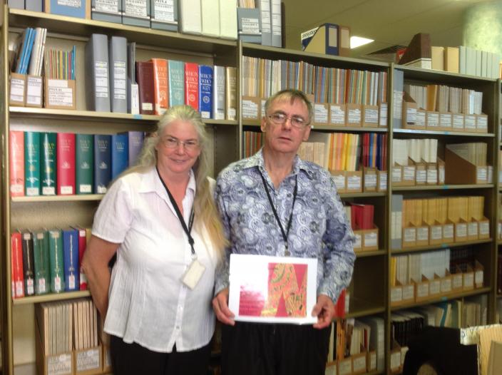 Christine and Ian standing in front of a bookcase. He is holding a certificate.